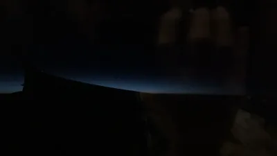 An airplane wing silhouetted against a faint blue horizon