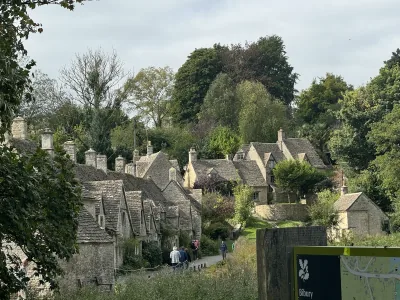 Stone cottages lining a village lane in Bibury, surrounded by trees and gardens