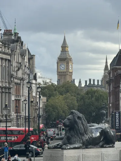 Big Ben framed by a London street, with a bronze lion and red buses in the foreground