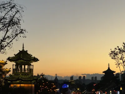 Traditional temple rooftops and a church cross silhouetted against the sunset in Datong