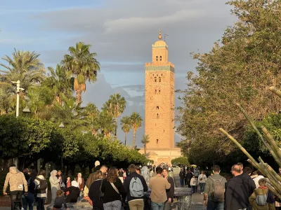 The sunlit minaret of Koutoubia Mosque rising above palm trees and visitors in Marrakech
