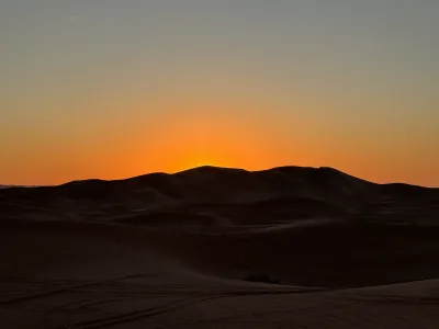 Sand dunes silhouetted against an orange sunset in Erg Merzouga, Morocco