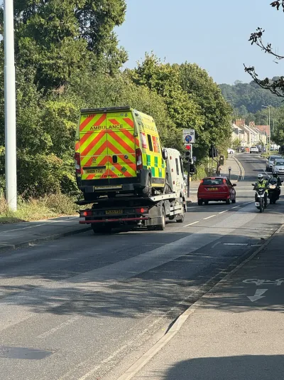 An ambulance being carried on a recovery truck along a street in Oxford