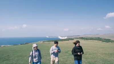 Three visitors walking across grassland with the white cliffs and sea behind them