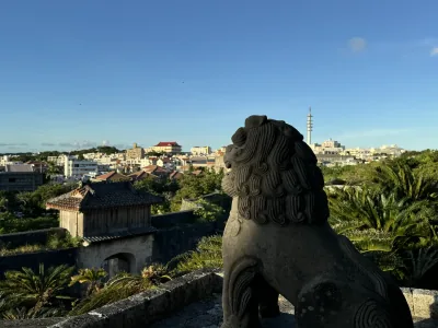 A stone lion overlooking a tiled gate and the city from Shuri Castle