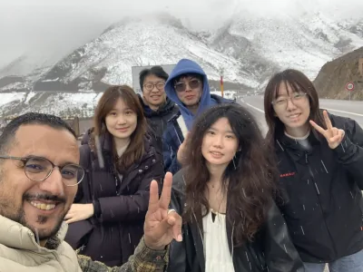 A group posing together in falling snow with the slopes of Tizi n'Tichka Pass behind them