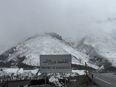 Snow-covered slopes at Tizi n'Tichka Pass beside the road and an Ouarzazate province sign